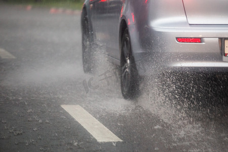 银色汽车的车轮在有选择的焦点下在日光城市中快速移动的雨水飞溅。