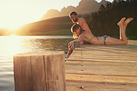 这里总是完美的一天……日落时分，一对穿着泳衣的恩爱年轻夫妇坐在码头上。