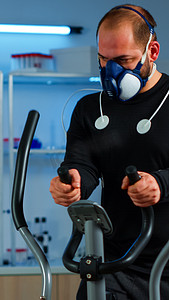 在交叉训练机上跑步的身体上贴有面罩和电极的运动员