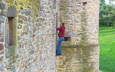 城堡上的窗户摄影照片_男人爬上城堡的墙壁。