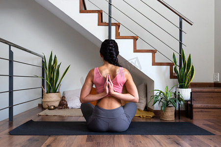 家里客厅摄影照片_在家里客厅做反向祈祷瑜伽姿势的女人的后视图。