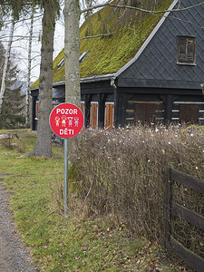 带有捷克文字的红色交通标志：Pozor deti - 在带苔藓屋顶的木屋前注意儿童。