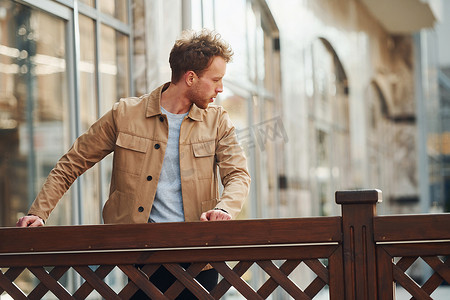 优雅的年轻人穿着正式优雅的衣服，靠在城市户外的木栅栏上