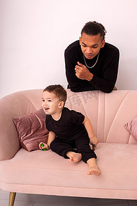 快乐的父亲和小儿子，穿着黑色衣服，坐在房间里浅粉色的沙发上，