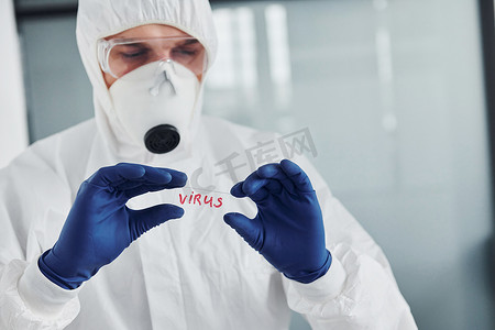 身着实验室外套、防御眼镜和面具的男医生科学家拿着玻璃，上面有病毒词