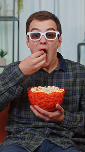 男人坐在沙发上吃爆米花，在家看有趣的电视连续剧、在线体育游戏