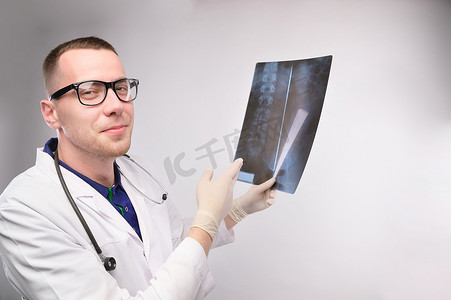 戴眼镜的年轻医生看着镜头，微笑着展示人体脊柱的 X 光片。
