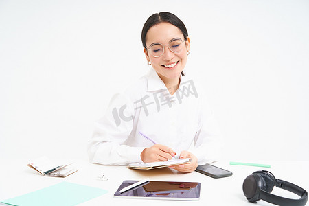 年轻导师的形象，亚洲女教师，坐在办公室，写作，在工作场所做报告，戴眼镜，白色背景