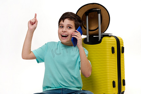 身穿蓝色 T 恤、带着黄色手提箱、在手机上聊天、用食指指着复制广告空间的青少年旅行男孩