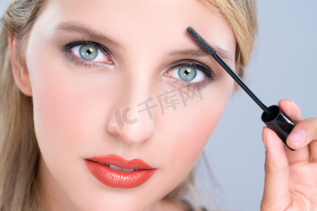 把卡摄影照片_特写美丽的女人把迷人的黑色睫毛膏放在长而浓密的睫毛上。