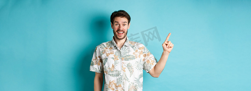 背景炫酷蓝色摄影照片_惊讶的快乐游客用手指指着空地，展示酷炫的促销，站在蓝色背景中的夏威夷衬衫