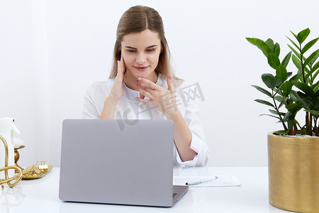 女医生在诊所办公桌前在笔记本电脑屏幕上与在线患者交谈的肖像，为家庭健康治疗提供在线咨询