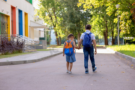 一个小女孩和一个男孩穿着白衬衫背着背包走在上学的路上。