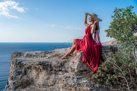 一位身穿红色长裙、头发飘逸的女孩坐在海面上的岩石上。