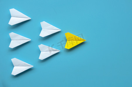 纸飞机的顶视图-黄色纸飞机折纸在蓝色背景上领先其他白色飞机。