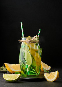 透明玻璃杯中的柠檬水，黑色背景中配有柠檬、酸橙、迷迭香小枝和薄荷叶