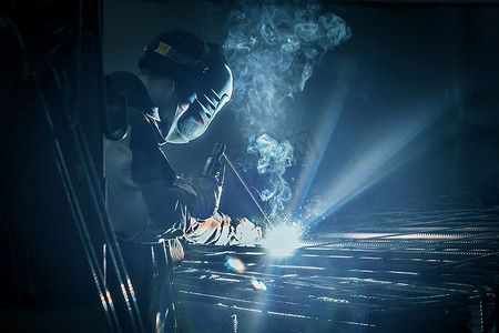 一名蒙面工人正在工厂或工业企业的金属结构上进行焊接工作