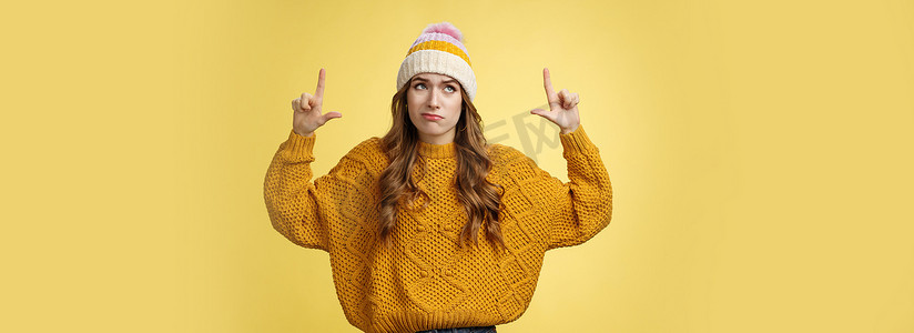 令人怀疑的不为所动的挑剔傲慢的 20 多岁欧洲女孩穿着帽子毛衣假笑犹豫不高兴举起食指 ip 看起来很失望表达轻蔑，站在黄色背景