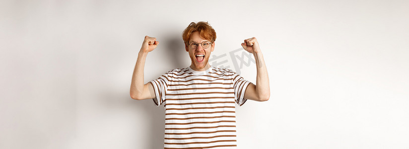 快乐的红头发人像赢家一样举起手来，获奖庆祝，欢呼雀跃，站在白色背景上