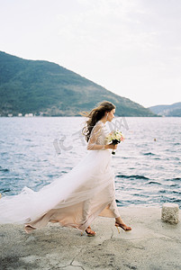 新娘在风中飘扬的礼服沿着码头走