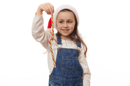 带条纹的红色和绿色糖果手杖，白色背景中模糊微笑的可爱小女孩手中的甜棒棒糖