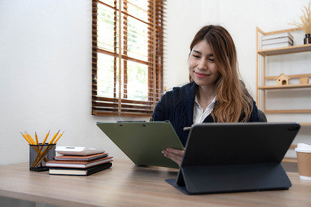 亚洲女性使用笔记本电脑，在办公室工作，在办公桌上使用计算器文档，进行规划分析财务报告、商业计划投资、财务分析概念。