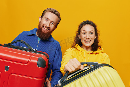 女人和男人微笑着，手里拿着手提箱，黄色和红色的手提箱愉快地微笑着，弯曲着，黄色背景，去旅行，家庭度假旅行，新婚夫妇。