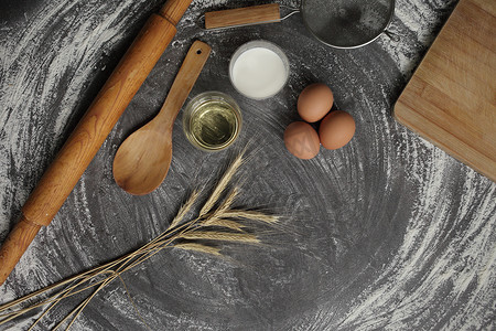 鸡蛋、面粉、橄榄油、牛奶、小麦耳朵、灰色桌子背景的厨房工具。