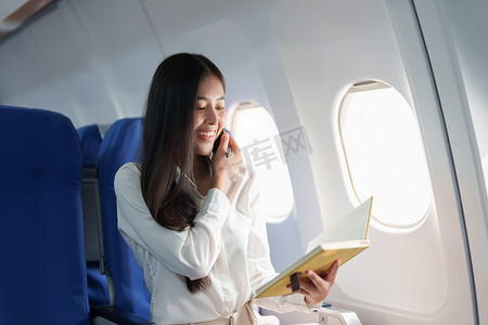 亚洲商务女性乘客坐在商务舱豪华飞机上工作时使用智能手机移动通话并在旅行时使用笔记本概念