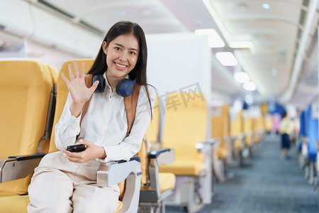 年轻的亚洲美女乘飞机旅行，乘客戴着耳机把手提行李放在飞机座位上方的储物柜里