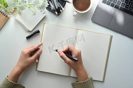 空白笔记摄影照片_女性手持笔在空白笔记本上书写的俯视图，做重要笔记或议程计划