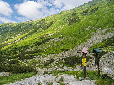 在山谷 Smutna dolina 的人行道上，有岩石巨石、灌木松和绿色山峰的小径路标。