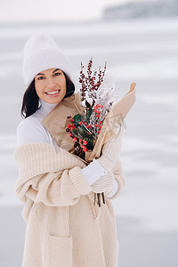 一个穿着米色开衫和冬花的女孩在下雪的季节在大自然中漫步。