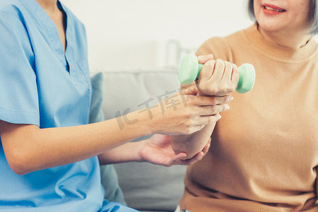 照顾者在家里用哑铃帮助心满意足的老年妇女锻炼。