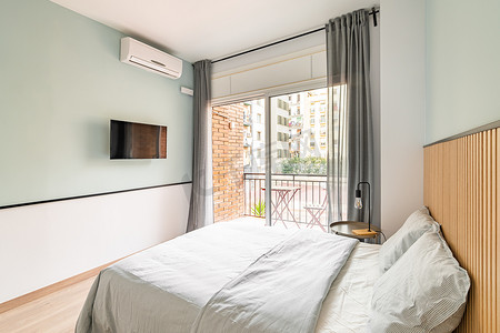 小而宜人的卧室配有一张带白色床单的双人床、电视和一个开放式露台，在阳光明媚的夏日俯瞰住宅区或旅游酒店的庭院
