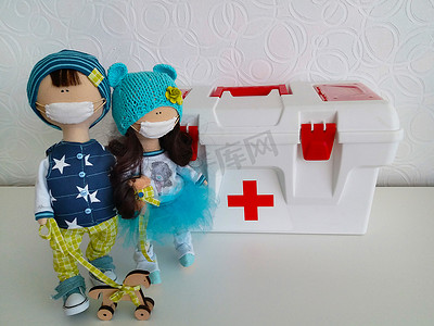 两个玩偶，一个男孩和一个女孩，站在一个大急救箱旁边。纹理或背景
