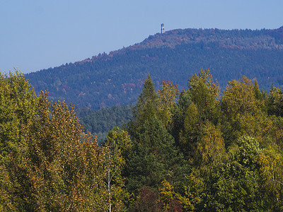 hory摄影照片_有秋天五颜六色的森林的草甸和有 Hvozd 或 Hochwald 了望塔的树木和山丘以及 luzicke hory 山的蓝天景观