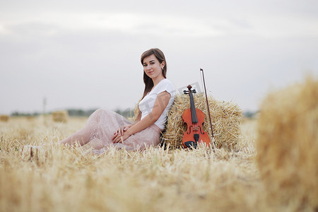 拿小提琴摄影照片_浪漫的年轻女人，头发飘逸，手里拿着小提琴，在田野里