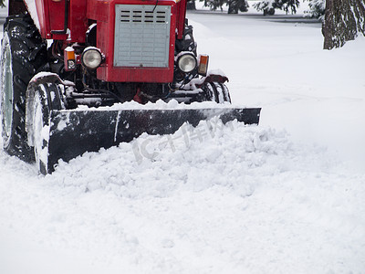 除雪摄影照片_拖拉机在降雪后从城市公园的人行道上除雪