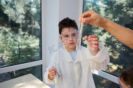 穿着实验室外套和护目镜的少年男学生，在化学课上仔细观察和分析试管中的溶液