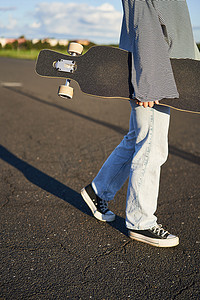 青少年溜冰女孩的短片，手拿着长板，在水泥路上用滑板行走