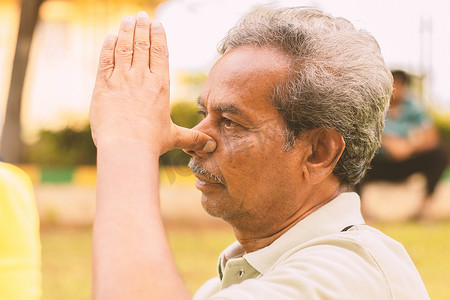交替摄影照片_老人在公园做交替鼻孔呼吸运动或 nadi shodhana pranayama 的特写-健康活跃的老年人生活方式的概念。