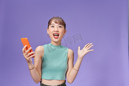 哇塞的表情摄影照片_年轻的亚洲女性手里拿着电话，脸上带着惊讶的表情