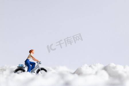 微型人物：在雪地背景上骑自行车的旅行者