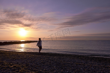 场景长图背景摄影照片_男孩在黎明时分在沙滩上玩鹅卵石