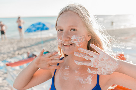 海滩背景下，一位年轻积极的金发女郎的肖像，她的脸和身体都涂有防晒霜，具有欧洲外表