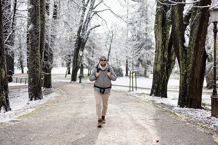 冬季，运动型父亲带着他的婴儿儿子穿着冬季连身衣和背包背带在城市公园散步