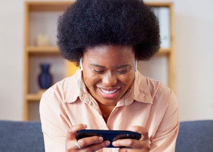 一位女士在家里的休息室里以横屏模式在手机上玩手机游戏。