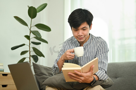 快乐的千禧一代男人在舒适的客厅里喝咖啡并检查他的工作计划