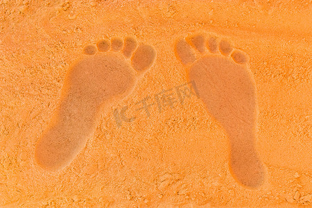 沙滩背景摄影照片_从男人的脚在橙色沙滩背景上的足迹特写